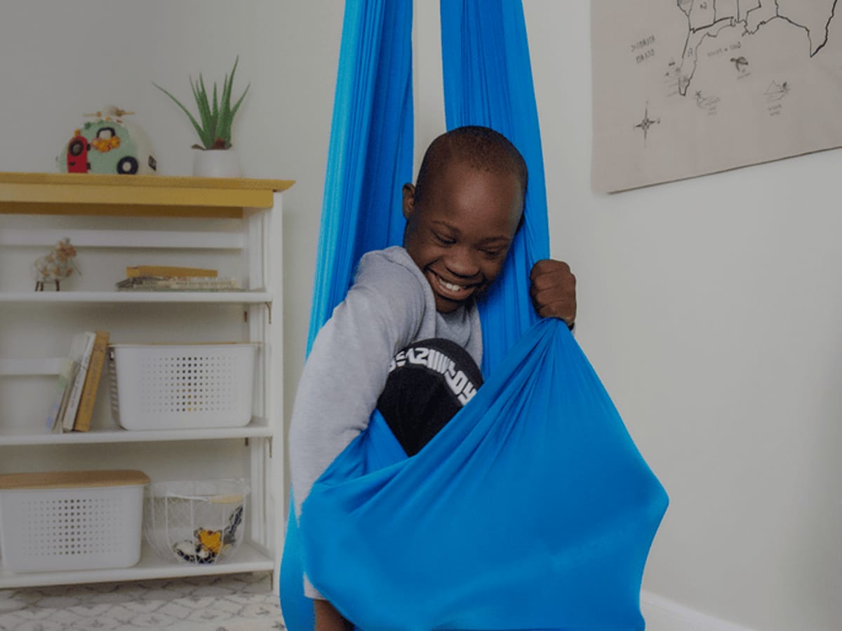 A child smiling inside a blue Harkla compression sensory swing